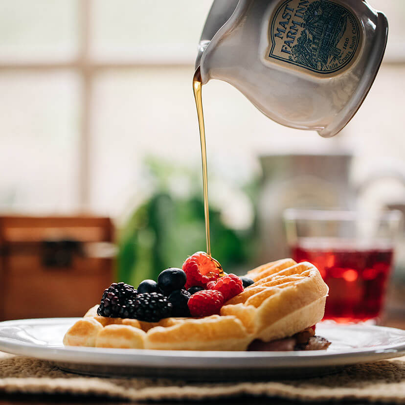 syrup being poured over a waffle with fruit