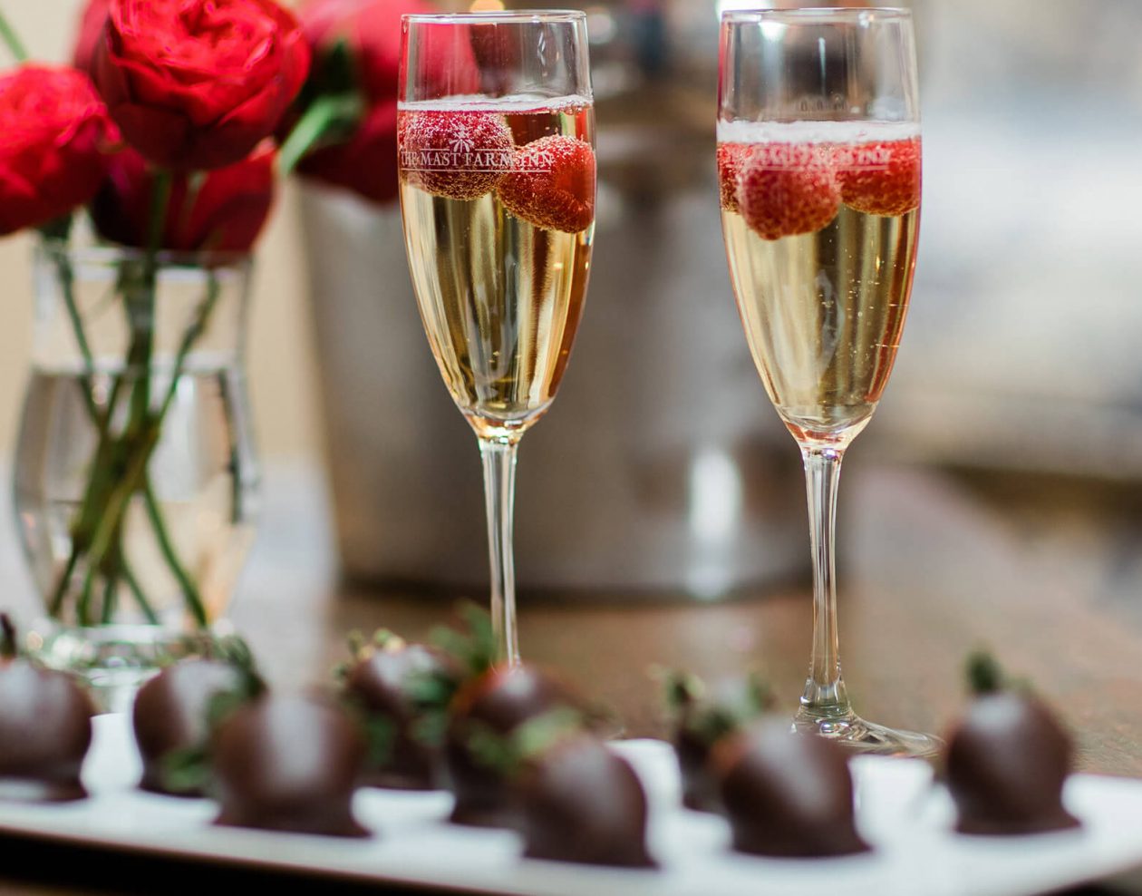 Chocolate covered strawberries and champagne with roses in the background