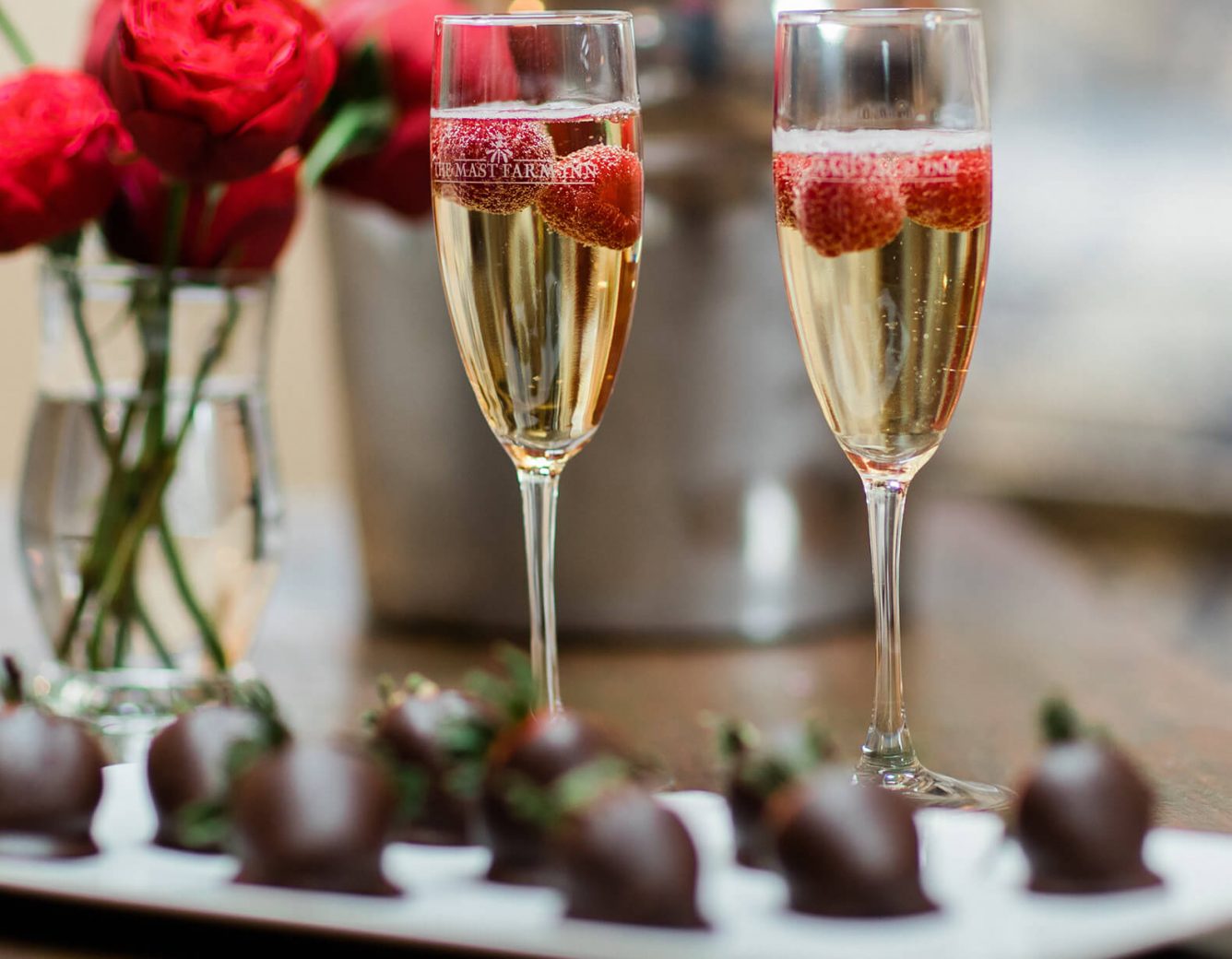 Chocolate covered strawberries and champagne with roses in the background