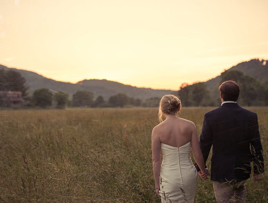 Newlyweds walking through a field at sunset